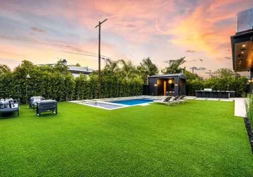 A modern backyard with a pool, lounge chairs, and outdoor seating area at sunset.