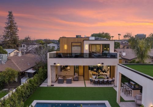 A modern two-story house with a pool and outdoor seating area at sunset in a suburban neighborhood.